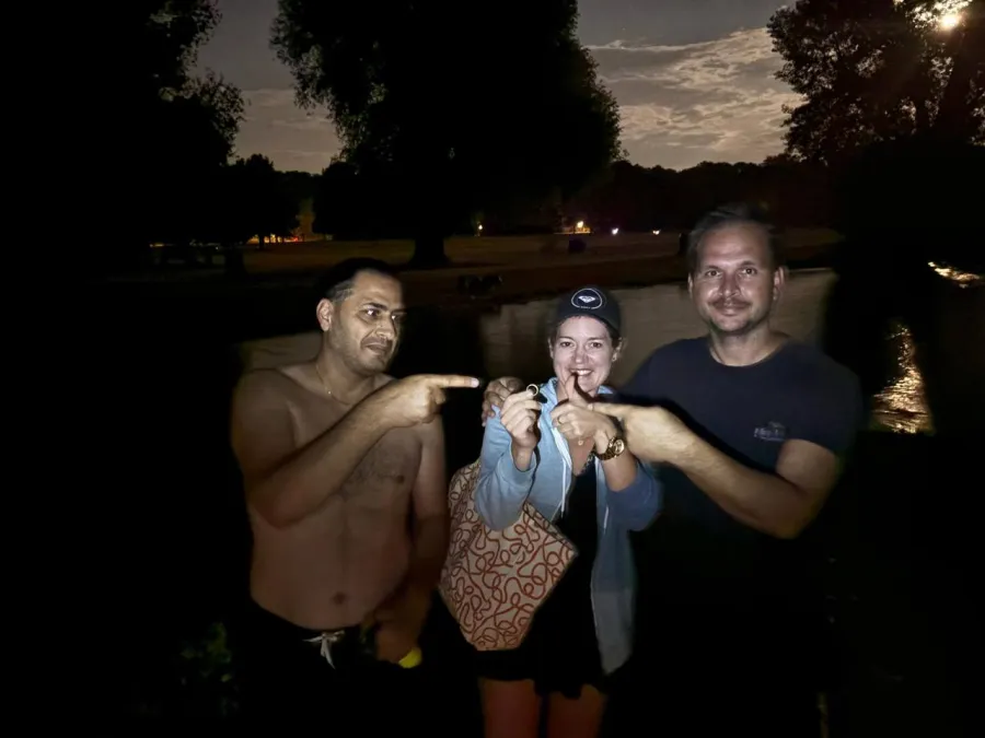 Drei Personen stehen abends am Schwabinger Bach im Englischen Garten, eine hält den wiedergefundenen Ring hoch